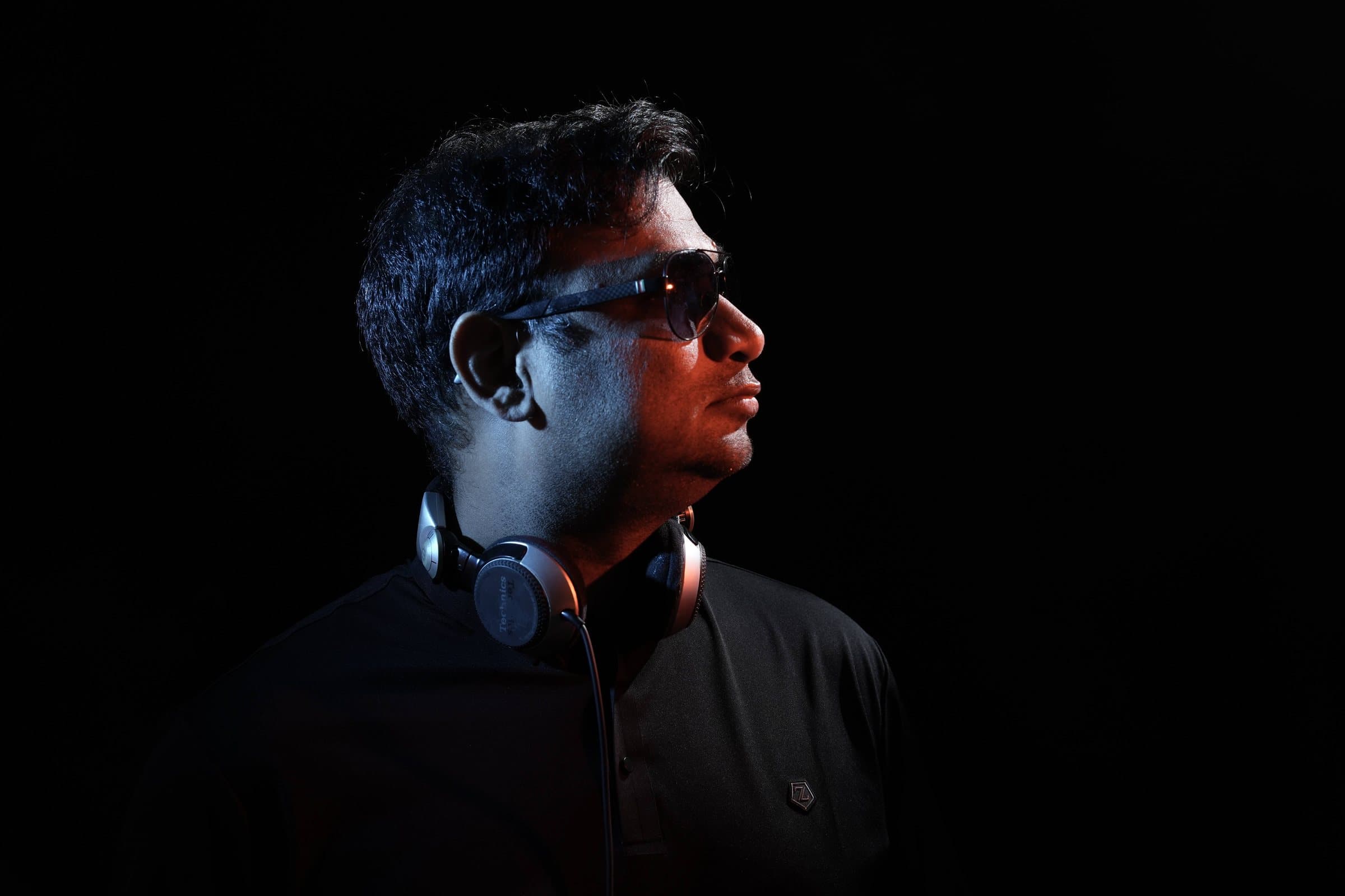 DJ Abdul in side profile, headphones around his neck, rim-lit in orange
